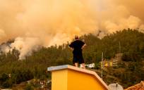Un vecino observa desde el tejado de una casa el incendio forestal declarado en la Palma. / E.P.