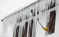 Una persona abre la ventana de su casa donde grandes carámbanos de hielo penden del tejado. EFE/ Jesus Diges
