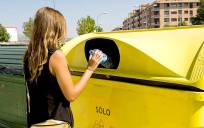 Una mujer introduce plástico en un contenedor amarillo.