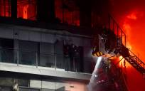 Un bombero trata de apagar el edificio en llamas con dos personas en un balcón, en el incnedio de Valencia. / Eduardo Manzana - E.P.
