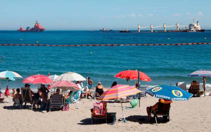 Imagen de archivo de este verano de unos bañistas en la playa de la Caleta, en Gibraltar, con el buque varado al Este del Peñón, el "OS 35". EFE/A. Carrasco Ragel