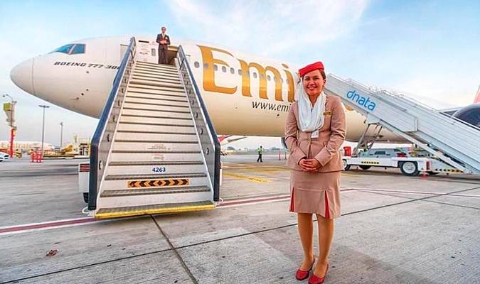 Una azafata junto un avión de Emirates. 