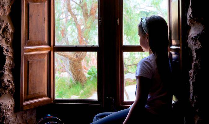 Una niña mirando por la ventana durante el confinamiento. / EFE