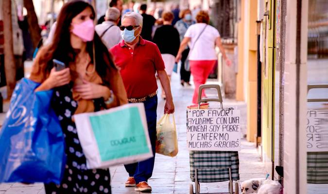 Viandantes pasan junto a un cartel colocado por una persona que ejerce la mendicidad en Sevilla. EFE/Julio Muñoz