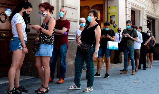 Decenas de personas protegidas con mascarilla hacen cola para entrar en una biblioteca, en Barcelona, durante el Día del Libro y de la Rosa. Marc Brugat / E.P.