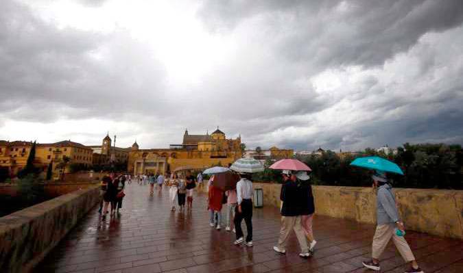 Personas pasean, paraguas en mano, este viernes bajo un cielo encapotado, por el puente romano de Córdoba. EFE/Salas