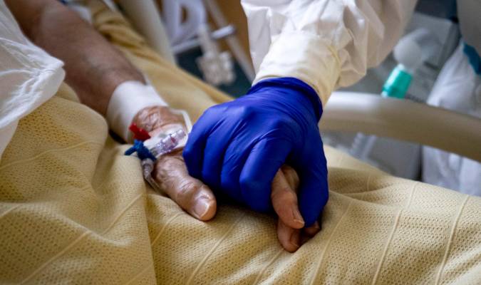 Un sanitario coge la mano de un enfermo de coronavirus. / Massimo Percossi - EFE