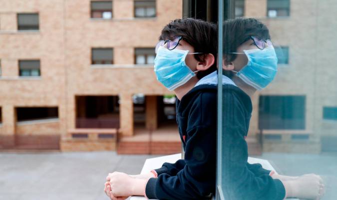 Un niño con una mascarilla se asoma a la ventana de su casa. / Óscar J.Barroso - E.P.