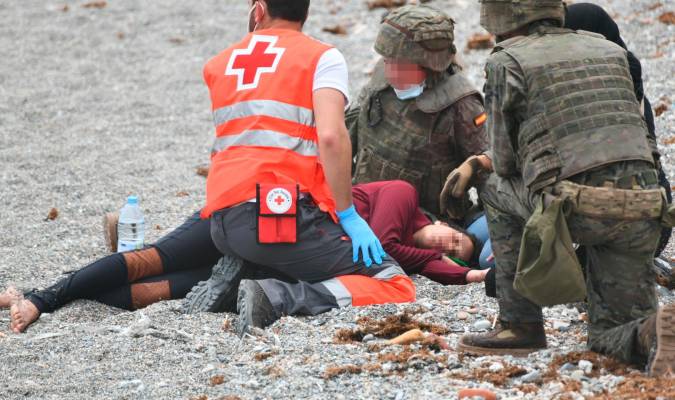 Un trabajador de la Cruz Roja y dos militares ayudan a una migrante que ha llegado a la orilla. / Antonio Sempere - Europa Press