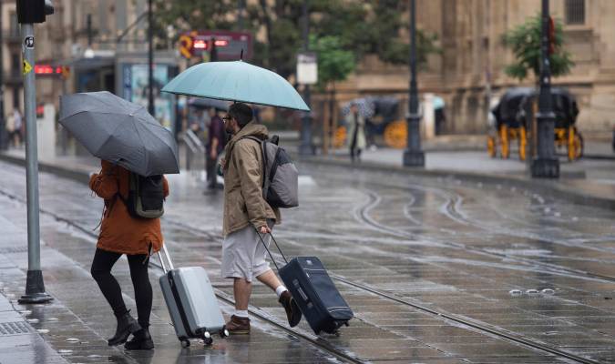 Una pareja con maletas se protegen de la lluvia bajo sus paraguas. / E.P.