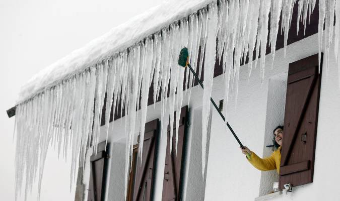 Una persona abre la ventana de su casa donde grandes carámbanos de hielo penden del tejado. EFE/ Jesus Diges