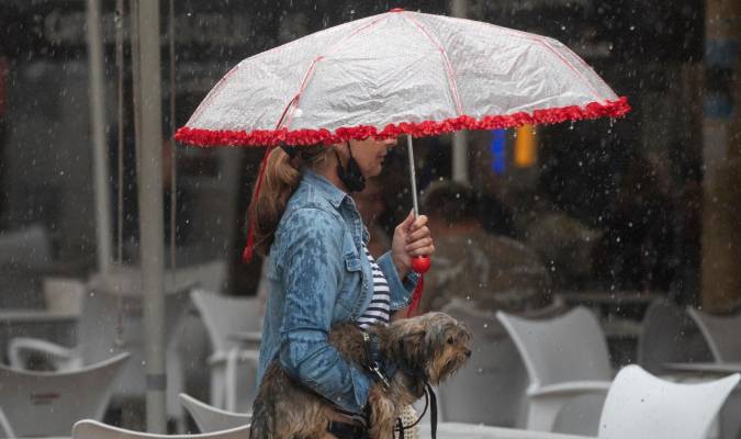 Una mujer lleva a su perro en brazos bajo una tormenta. / E.P.