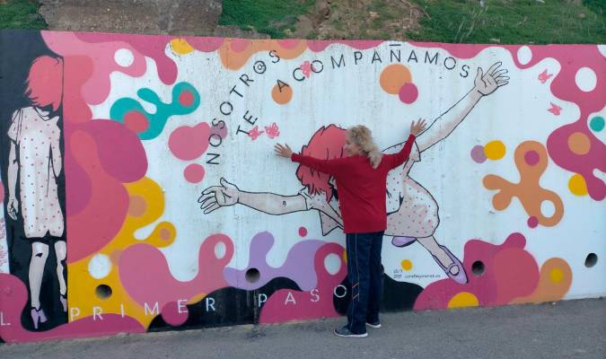 Pilar Domínguez se abraza al mural pintado en Gelves por su amiga Concha Jiménez. / El Correo.