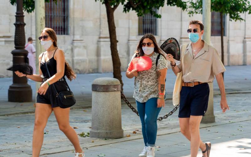  Tres jóvenes pasean con mascarillas y abanicos en Sevilla. / Eduardo Briones - E.P.