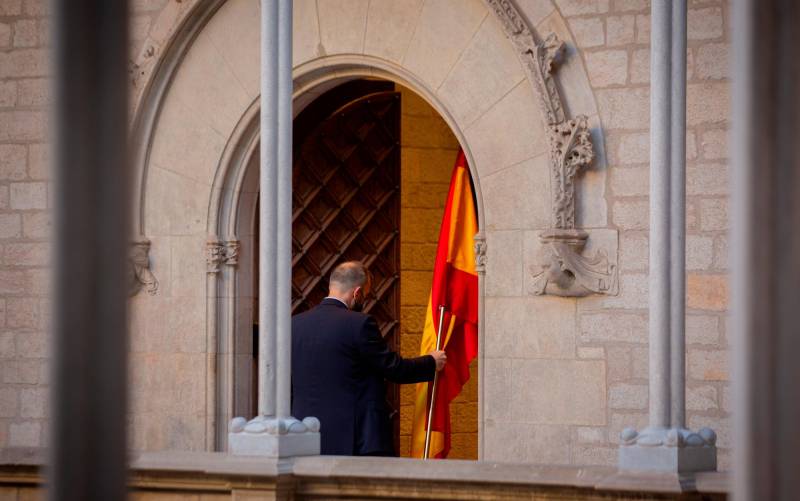 Un hombre retira la bandera de España antes de que el president de la Generalitat comparezca en rueda de prensa en el Palau de la Generalitat. David Zorrakino / Europa Press