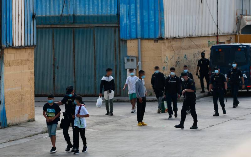 Agentes de la Policía Nacional acompañan a menores marroquíes a las naves acondicionadas anexas a la frontera del Tarajal. / Antonio Sempere / Europa Press