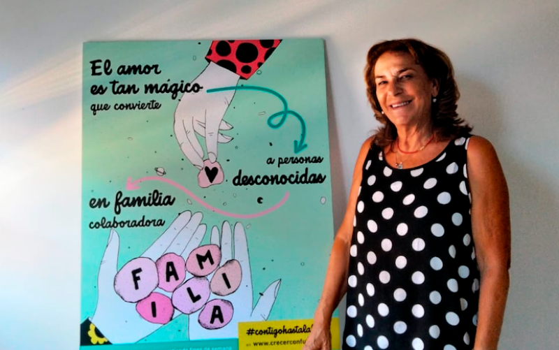 Encarnación Vega, presidenta de la ONG Crecer con Futuro, junto a uno de los carteles de la campaña para ampliar en Andalucía el número de familias colaboradoras que hagan acogimiento temporal de niños o niñas que están en centros de protección de menores.