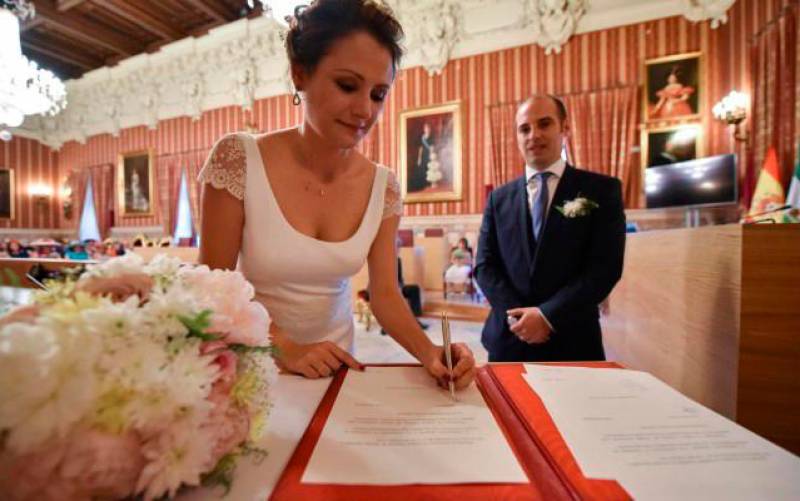 Una pareja firma el acta matrimonial tras contraer matrimonio en el Salón Colón del Ayuntamiento de Sevilla. / Jesús Barrera