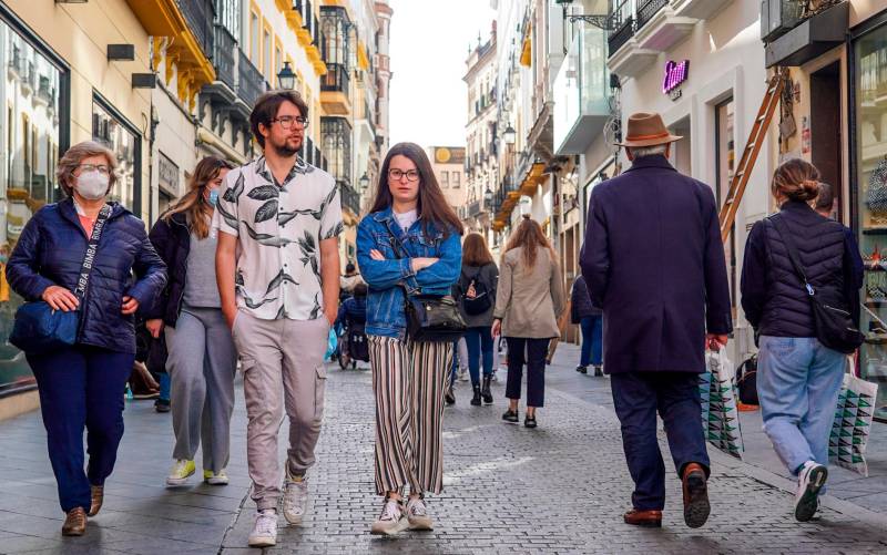 Una pareja sin mascarillas y otros ciudadanos con mascarillas por la calle Tetuán de Sevilla. / Eduardo Briones - E.P.